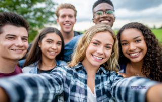 a group of six teenage boys and girls take a selfie outside with trees in the background