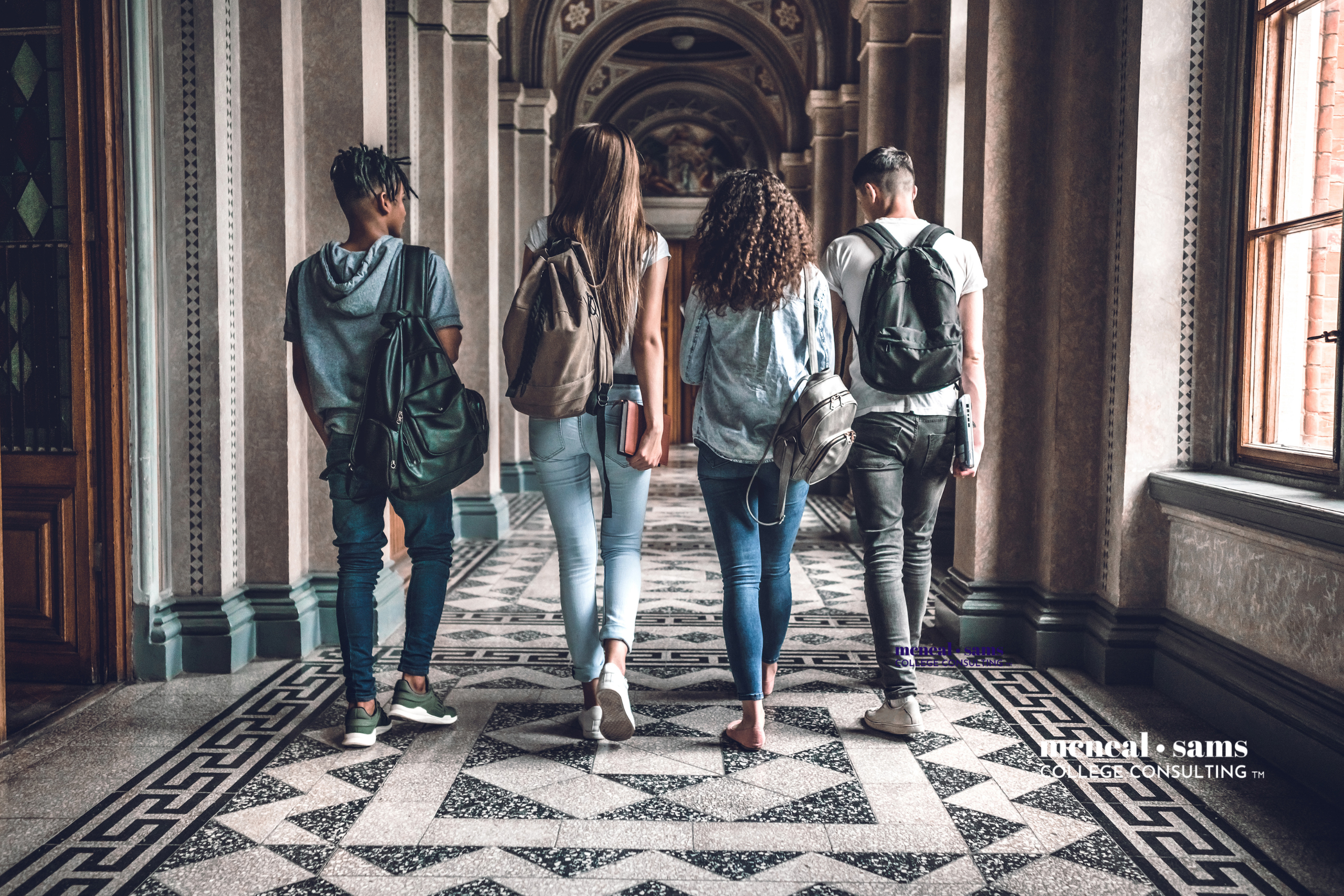 a group of four teenagers walk down a school hallway with backpacks on their shoulders