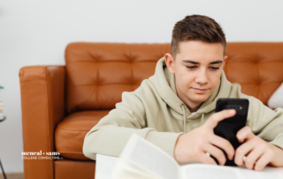Teenage boy sits on floor in front of leather couch and scrolls on his phone.