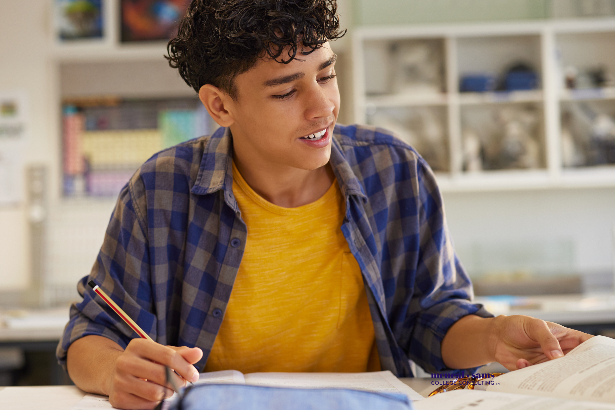 teenage boy is seated at a desk studying papers with a pencil in his hand