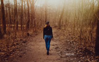 a woman with her back to the camera walking down a spook, foggy dirt path in the woods
