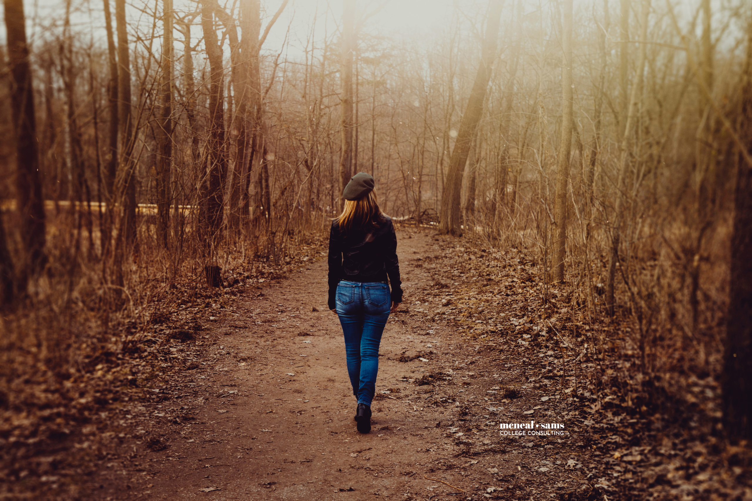a woman with her back to the camera walking down a spook, foggy dirt path in the woods