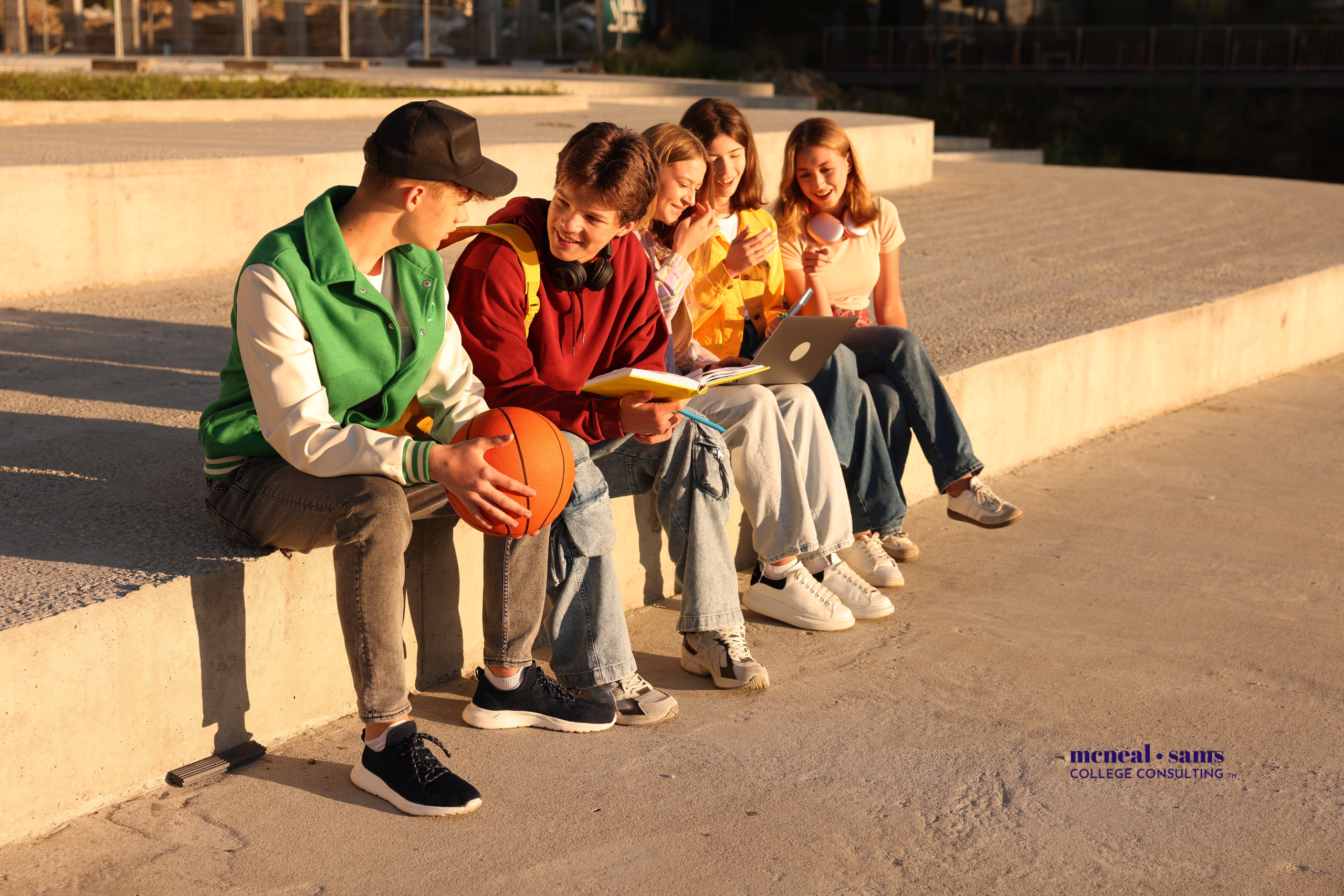 Two teenage boys and three teenage girls sit on step outside talking.