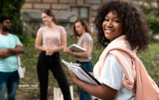 a group of four young adults stand on a college campus, holding books and talking to each other