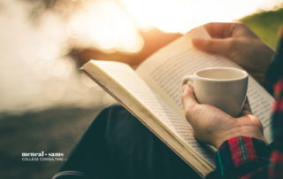 person is holding a cup of coffee in one hand and a book in their lap