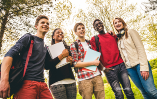 three teenage boys and two teenage girls huddle together smiling