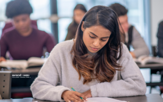male and female students are seating at desks in a classroom. they are writing in notebooks