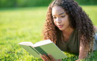 Teenage girl lies on grass reading a book