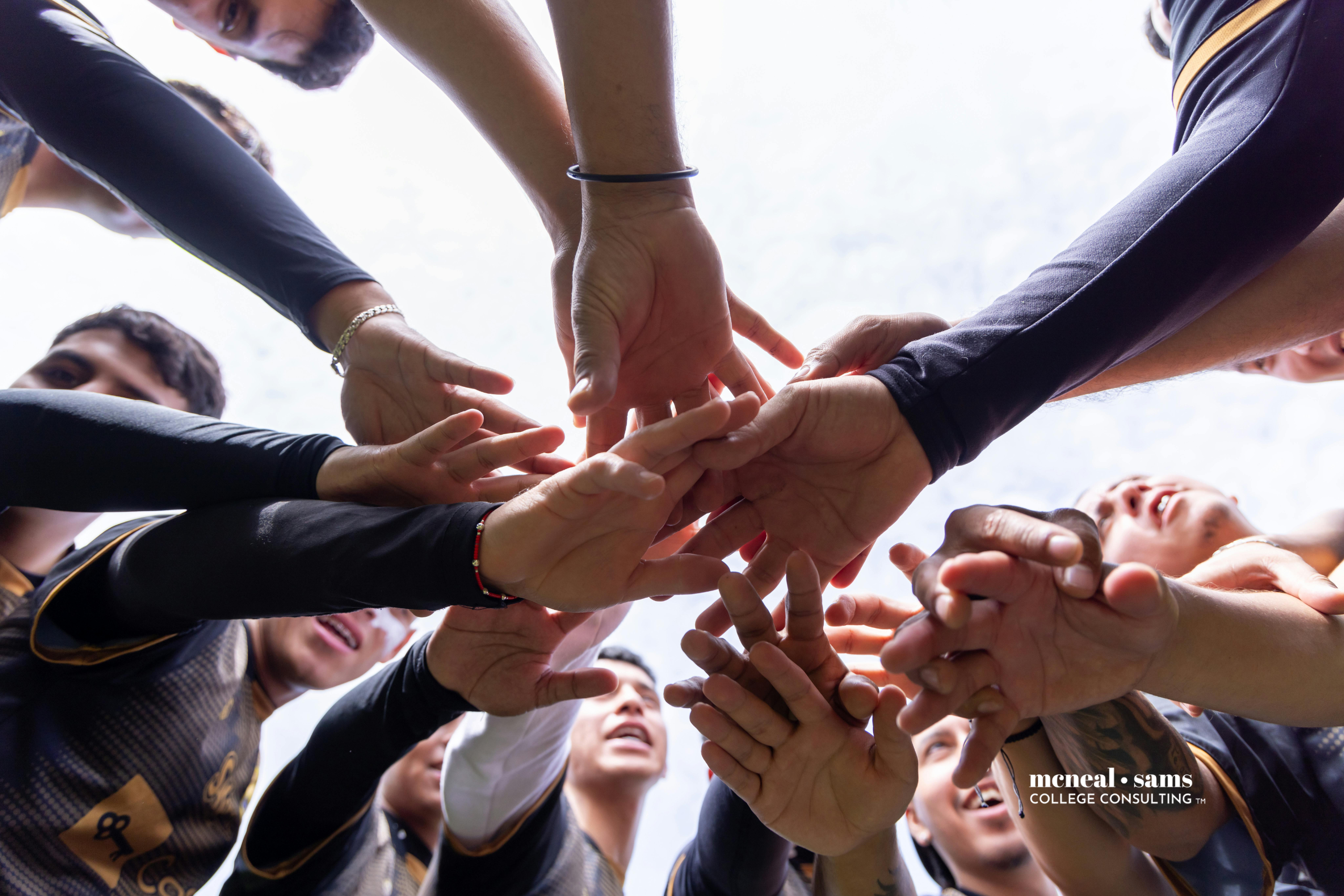 Teen boys are in a game day huddle with their hands in the middle of the huddle