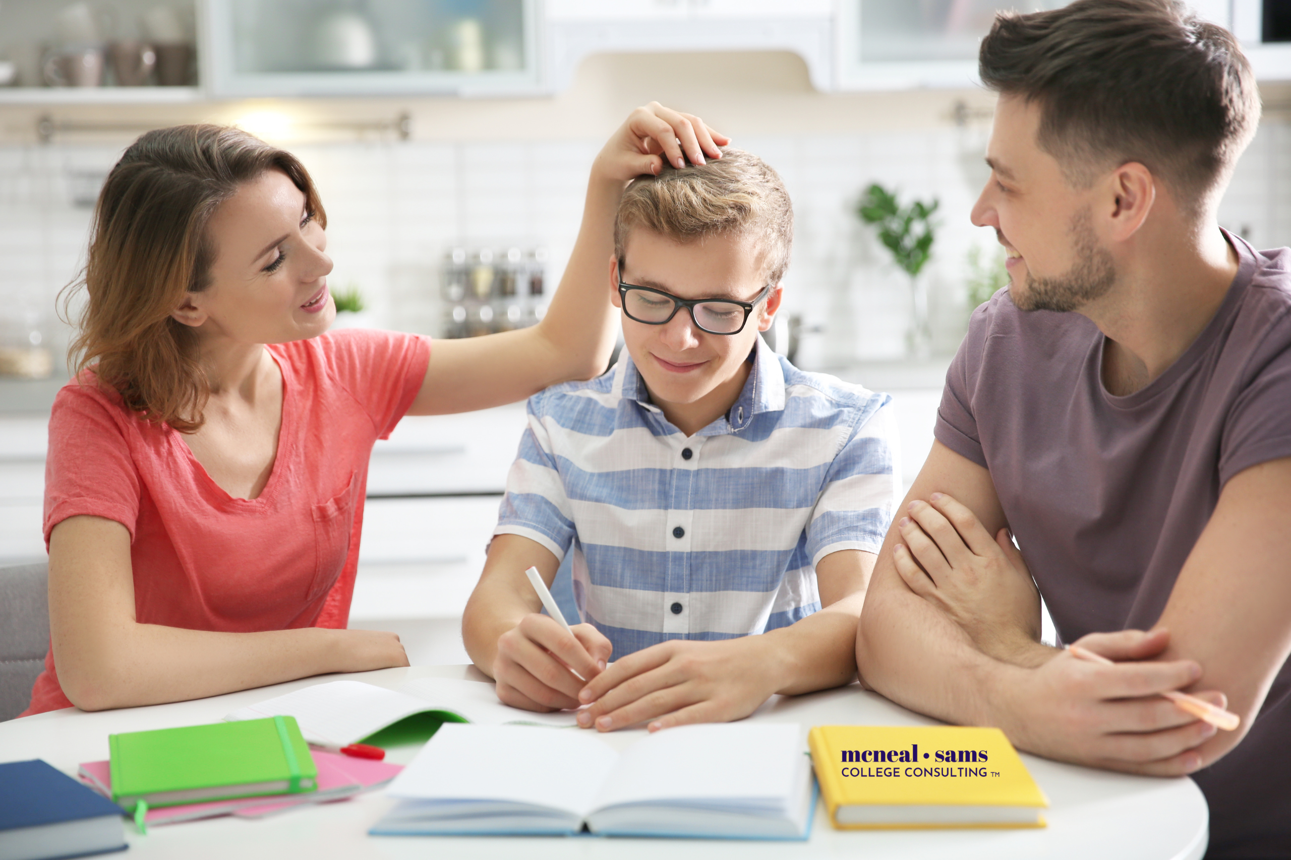 teenage boy sits with father and mother at a table while writing in a notebook